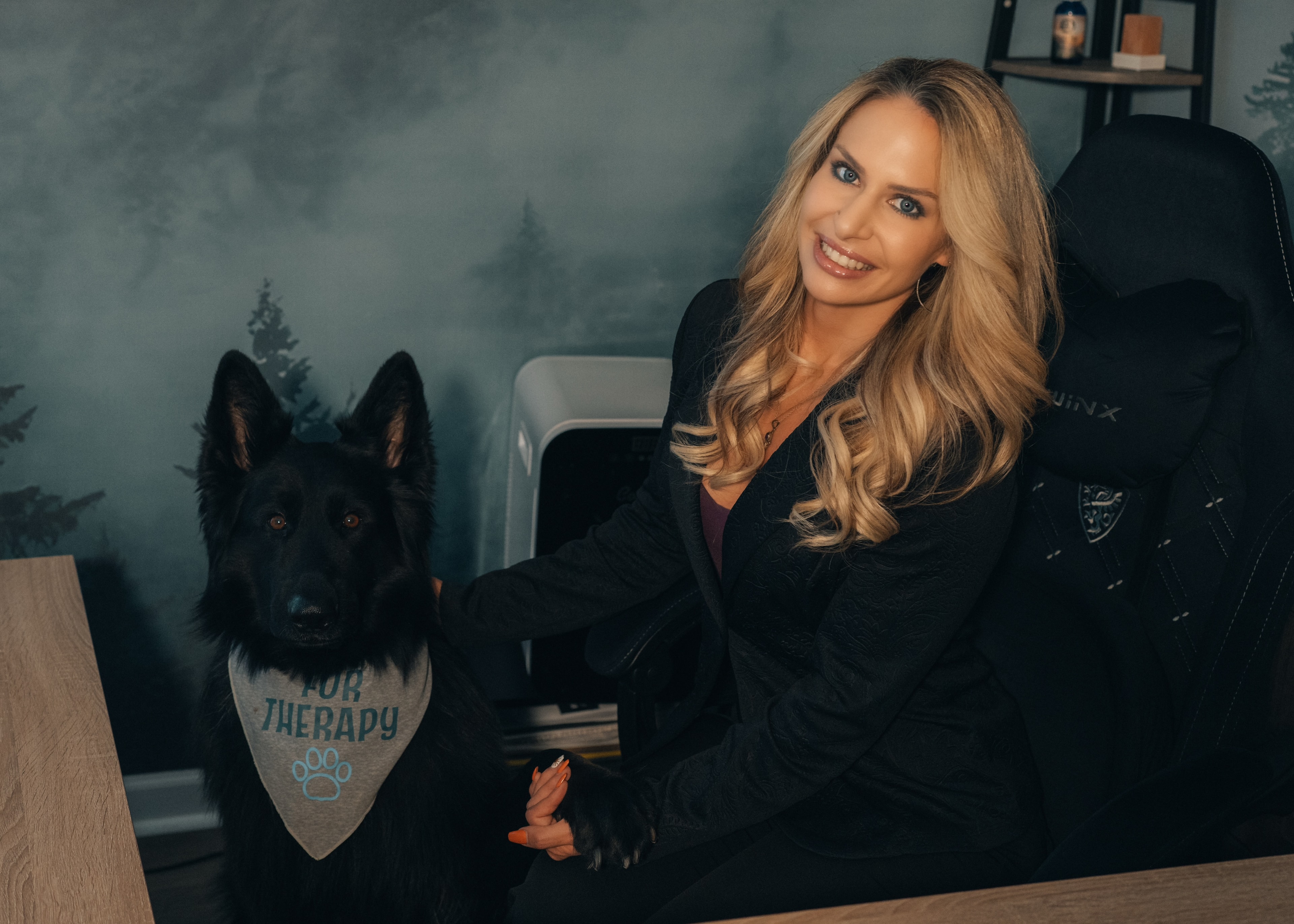 Roxanne Miller, LCSW, with her dog Thor, studio portrait with a soft forest backdrop